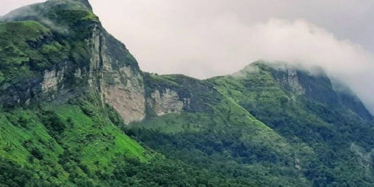 A mountain with lush green trees and clouds, showcasing the breathtaking view from Rani Jhari Edge Point in Kudremukh National Park.