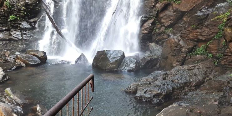 A waterfall cascades over rocks near a bridge, surrounded by lush forests in Kudremukh National Park.