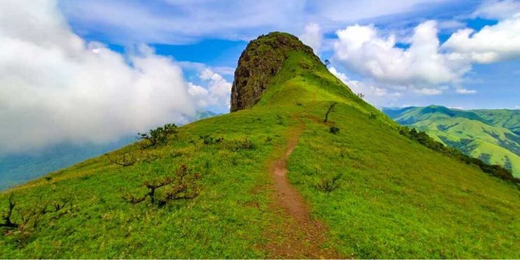 Grassy path leading to a mountain, with clouds in the sky, ideal for hiking in favorable seasonal conditions.