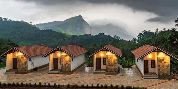Three small cabins nestled in front of a majestic mountain range, showcasing the serene beauty of Vanaba Hillview Homestay.