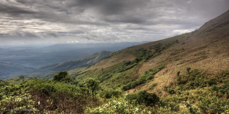A panoramic view of mountains and valleys from a hilltop in Balehonnur, surrounded by lush greenery and coffee estates.