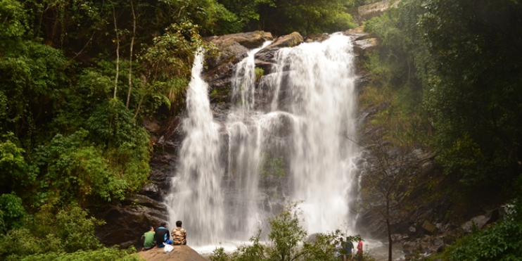 People standing near Alekan Falls in a lush forest, enjoying the scenic view of the cascading water.