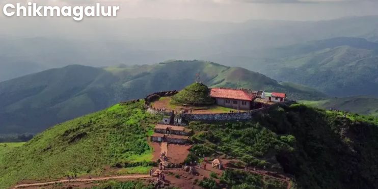 A small building perched on a mountain peak, surrounded by lush greenery and misty clouds in Chikmagalur, Karnataka.
