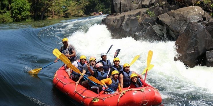 A group of people enjoying river rafting in an inflatable raft on a scenic river during the monsoon season.
