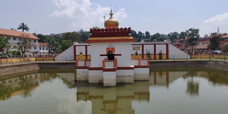 A small temple surrounded by water in a serene pond, reflecting Karnataka's rich heritage and spiritual ambiance.