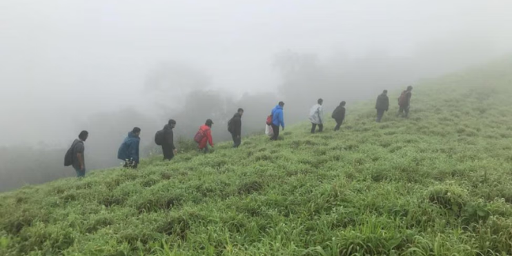 A group of hikers ascends a foggy hill at Jenukal Gudda, surrounded by lush greenery and the serene atmosphere of the Western Ghats.