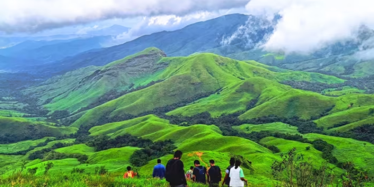 Three hikers navigate a lush green mountain trail during the Kudremukh Trek in Chikmagalur District, Karnataka.