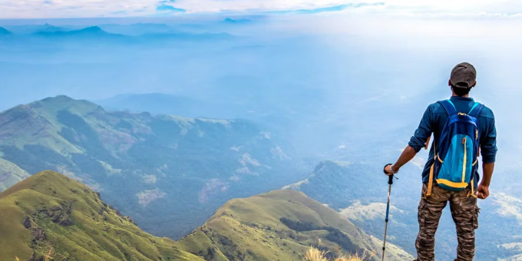 Man standing atop Nishani Motte mountain, equipped with a backpack and hiking poles, overlooking misty valleys.