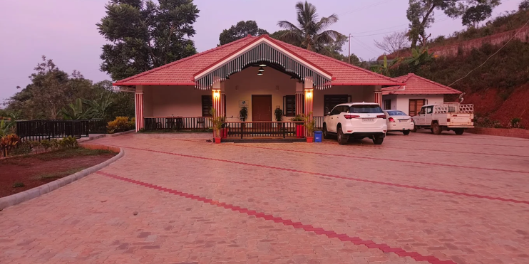 A house with a car parked in front, set in a lush, green landscape, ideal for a nature retreat in Mudigere.