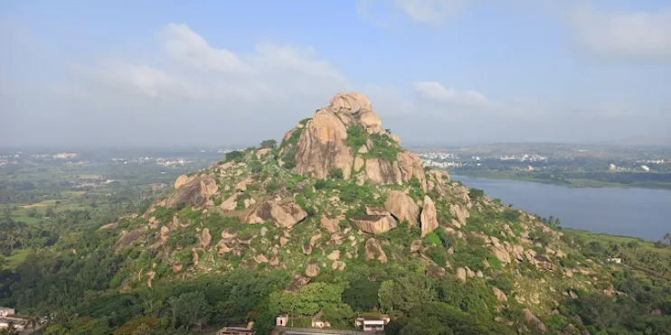 Aerial view of Kunti Betta's twin hills with a serene lake and paddy fields in the background, showcasing a scenic landscape.