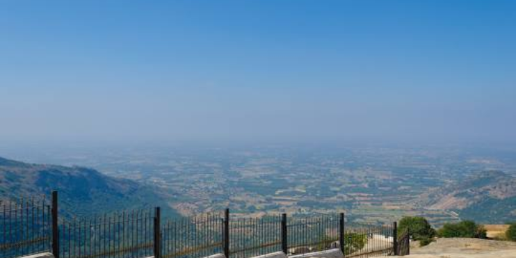 View from the top of Nandi Hills, showcasing misty valleys and distant hills under a clear blue sky. Perfect for sunrise.