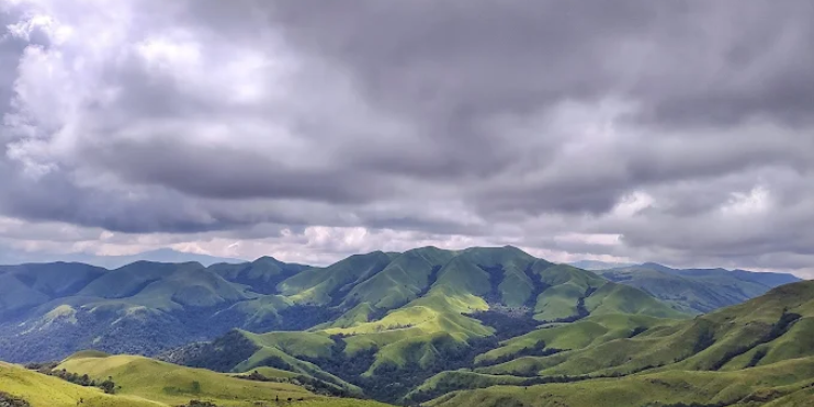 A scenic view of mountains shrouded in clouds, showcasing the beauty of Kyatanamakki Hill at sunrise.
