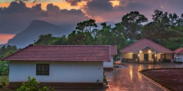 A house at sunset with a mountain backdrop, symbolizing tranquility at Vanaba Hillview in Chikmagalur.